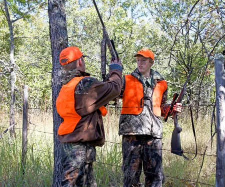 Two young hunters properly passing firearms over a fence.