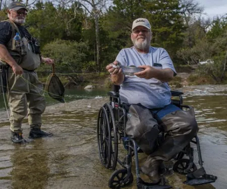 Man in wheel chair holding a rainbow trout.