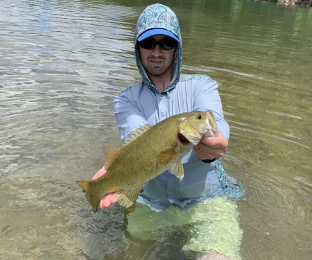 Person holding a smallmouth bass in creek.