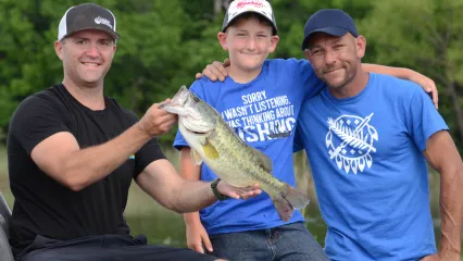 Three people in a boat with a recently caught bass