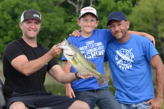 Three people in a boat with a recently caught bass