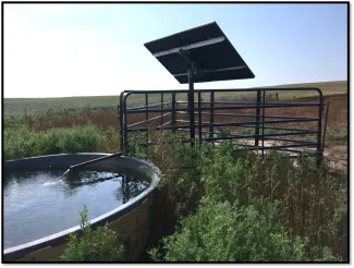 A solar panel is installed as part of a well that fills a nearby stock tank.
