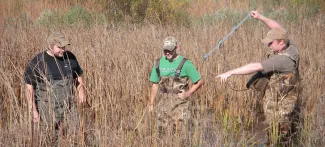 Three students with waders stand in a wetland unit while one student holds an antenna. 