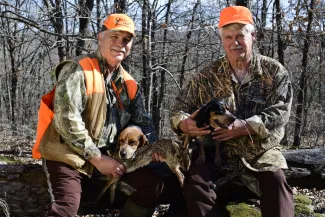 two hunters pose with their dog and a harvested rabbit