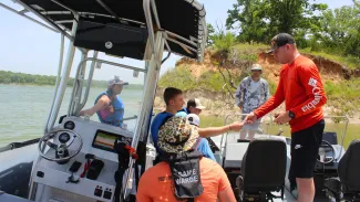 Campers are in a boat learning how to be a game warden by checking the fishing license of an Oklahoma angler..