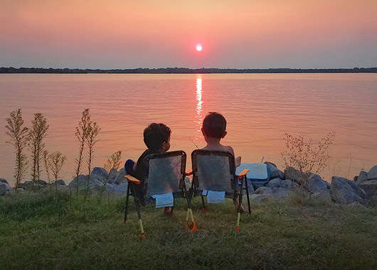 Two boys watching the sunset over a lake