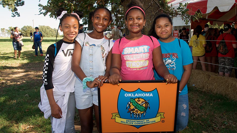 A group of young girls standing in front of a agency logo at Wildlife EXPO.