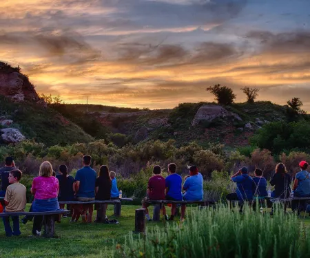 People sitting on benches looking at the horizon waiting for bats to fly over at Selman Bat Caves.