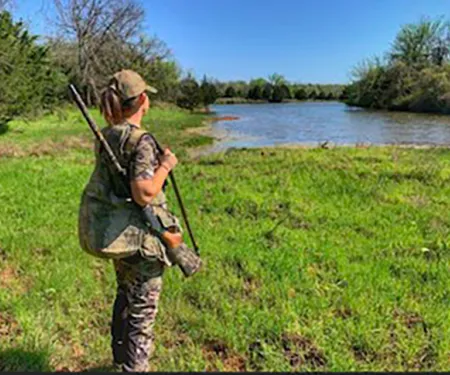 Woman in field with shotgun.