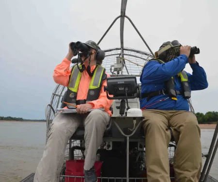 Biologist on airboat with binoculars.