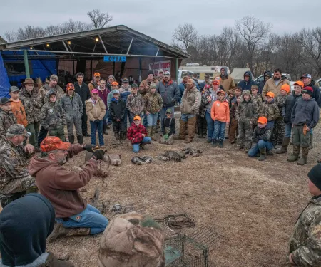 A group of people listen to a man demonstrating trapping methods. 