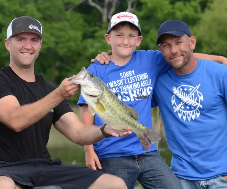 Three people in a boat with a recently caught bass
