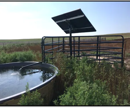 A solar panel is installed as part of a well that fills a nearby stock tank.