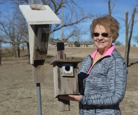 A woman stands next to a nest box while holding another nest box in her hands. 