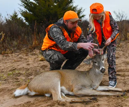 A man and his niece (both wearing hunter orange) are looking at and discussing about the deer that the niece recently harvested.