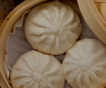 Three steamed buns in a bamboo container.