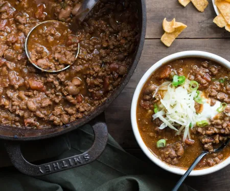 A pot of chili next to a bowl of chili.