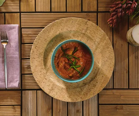 Bowl of Butter Pheasant curry garnished with herbs, on a rustic table with cutlery, a napkin, and decor.