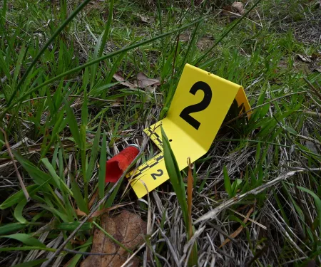 A photograph of poaching evidence. A yellow evidence marker with the number two on it is next to an empty shotgun shell on grass.