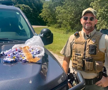 Oklahoma Game Warden Gillham stands next to evidence of snake skins piled on his  truck's hood.