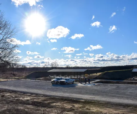 A shooting range with two roof-covered benches and vehicles in the parking lot
