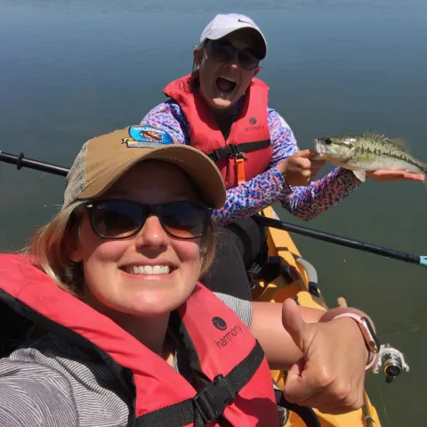 Two women fishing from a kayak with a bass.