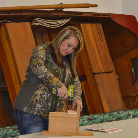 A woman attaches the predator guard to a wooden nest box. 