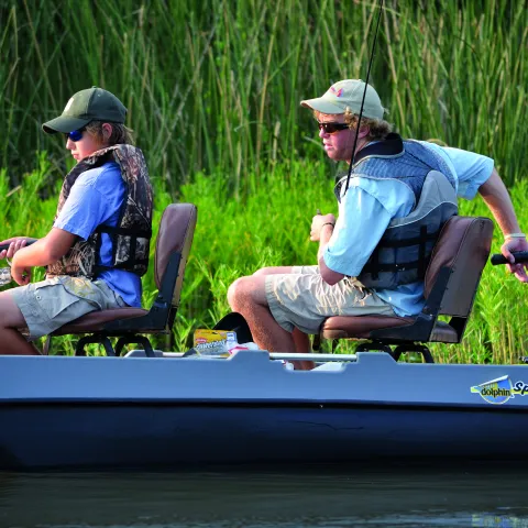 Two anglers sit in a boat with life vests on.