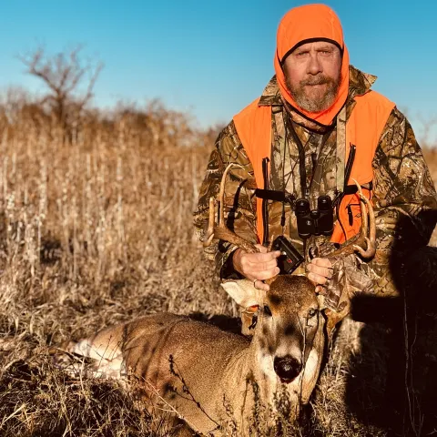 Hunter wearing orange pictured with a harvested deer.