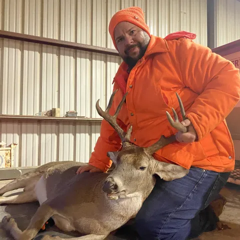 Hunter wearing orange pictured with a harvested deer.