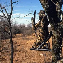 Hunter in camo in a tree stand with a bow.