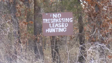 A brown sign with white lettering shows "No Trespassing Leased Hunting." 