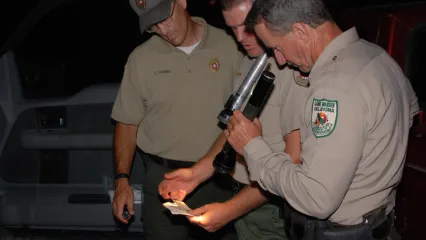Three Game Wardens look at a license by flashlight.