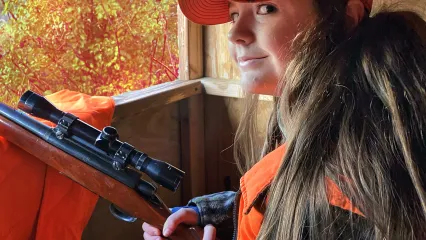 young lady sitting in deer blind holding rifle