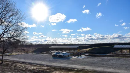 A shooting range with two roof-covered benches and vehicles in the parking lot