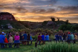 People sitting on benches looking at hills with a horizon above.