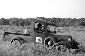 Old black and white photo of agency truck in field.