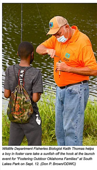 Wildlife Department Fisheries Biologist Keith Thomas helps a boy in foster care take a sunfish off the hook at the launch event for "Fostering Outdoor Oklahoma Families" at South Lakes Part on Sept. 12. (DON P. BROWN/ODWC)