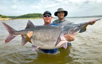 Angler James Lukehart of Edmond holds the potential world-record American paddlefish that he snagged June 28, 2020, at Keystone Lake. This 146.7-pound monster bested the month-old state record held by Jeremiah Mefford, who is also in this photo and was serving as Lukehart's fishing guide. (Photo by Jason Schooley/ODWC)