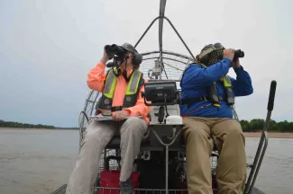 Biologist on airboat with binoculars.