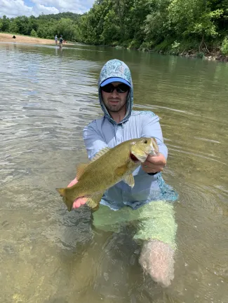 Person holding a smallmouth bass in creek.