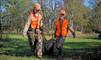 Mother and daughter bring harvested buck back from the field.  Photo by legendary ODWC photographer Steve Webber.