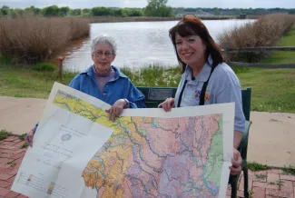 Two women sit on a bench with a map of Oklahoma