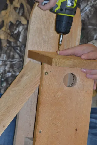 A woman attaches the roof of a wooden nest box. 