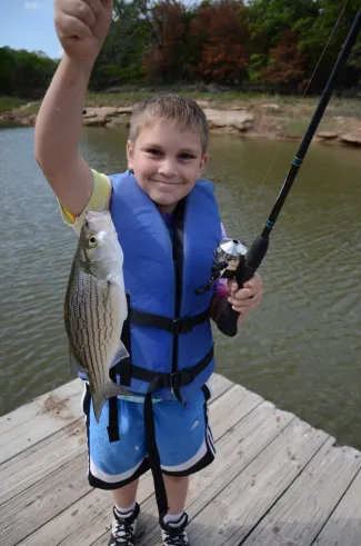 A boy stands on a dock with a fish.