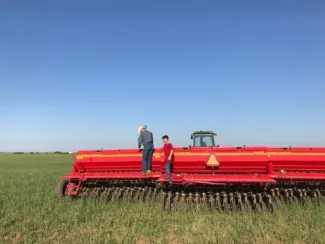 Two people stand next to a tractor implement. 