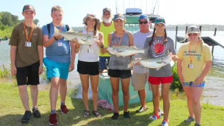 A group of smiling teens holding their caught fish at ODWC's Wildlife Youth Camp.