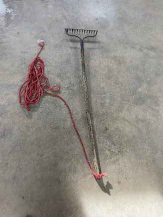 A red rope is tied to a wooden garden rake