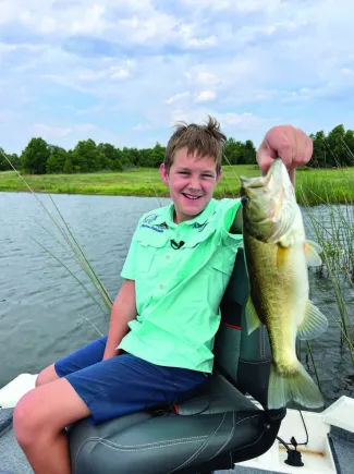 A young man sits in a bot holding a large fish. 