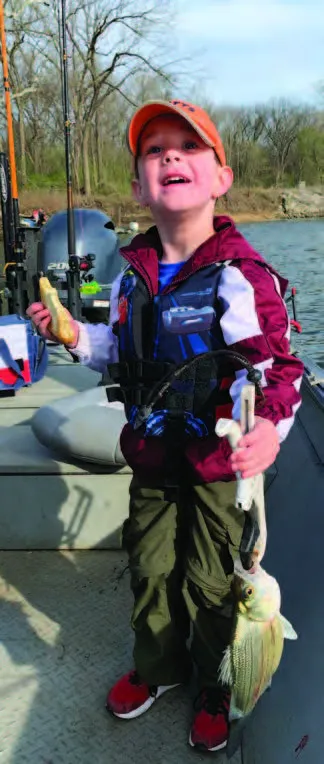 A young boy stands on a boat and holds a fish. 